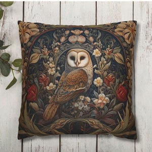May include: Square decorative pillow featuring a detailed illustration of a barn owl surrounded by flowers and foliage. The owl has a white face and brown feathers, set against a dark background with floral accents in shades of red, cream, and green.