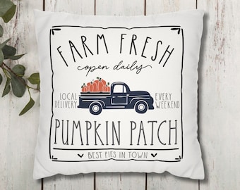 May include: White pillow with a black and white graphic design of a truck carrying pumpkins. The text reads "Farm Fresh open daily Local Delivery Every Weekend Pumpkin Patch Best Pies in Town".