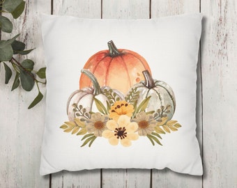 May include: A white pillow with a watercolor design of three pumpkins and fall flowers. The pumpkins are orange, white, and green. The flowers are yellow and white.