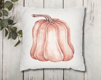 May include: A white pillow with a watercolor illustration of a peach-colored pumpkin. The pumpkin has a stem and is in the center of the pillow.