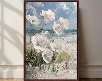 May include: A framed painting of white flowers with yellow centres, set against a beach scene. The artwork features a blue sky with clouds and a view of the ocean. The painting is in a dark brown frame and rests on a wooden floor.