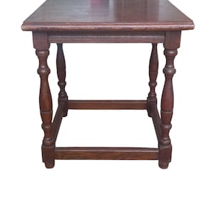 Può includere: Tavolino quadrato in legno, finitura marrone scuro. Il tavolo ha un piano piatto e quattro gambe tornite collegate da traverse. Il tavolo è alto circa 61 cm e largo 51 cm.