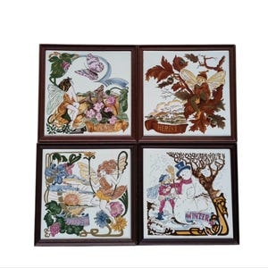 May include: Four framed ceramic tiles depicting the seasons. Each tile features a fairy with floral and seasonal elements. The frames are dark brown. The tiles are white with colourful illustrations.