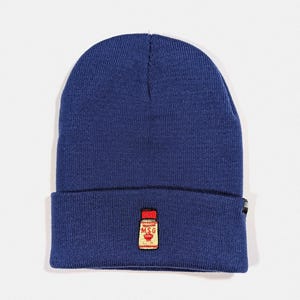May include: A navy blue beanie with a small embroidered image of a red and yellow MSG seasoning bottle.