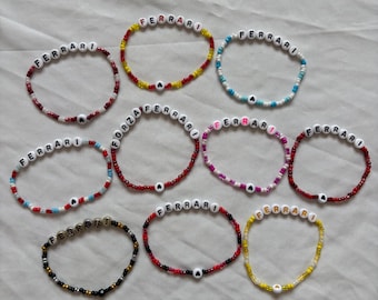 Puede incluir: Diez pulseras circulares de cuentas con letras blancas que forman la palabra Ferrari o Forza, intercaladas con pequeñas cuentas de vidrio de colores. Las pulseras presentan varias combinaciones de colores como rojo, amarillo, azul, negro y blanco, algunas con cuentas en forma de corazón.