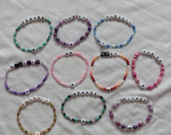Puede incluir: Diez pulseras de cuentas hechas a mano con cuentas de letras blancas que deletrean nombres como George, Russell y GR63, intercaladas con cuentas de vidrio, metálicas y de acabado perlado. Cada pulsera incluye una pequeña cuenta en forma de corazón.