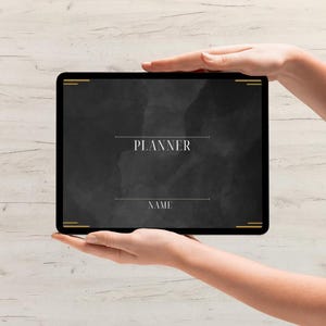 Puede incluir: Una tableta negra con detalles dorados muestra la palabra "PLANNER" en una fuente serif, con un espacio para un nombre debajo. El fondo es un diseño oscuro de acuarela. La tableta está sostenida por dos manos.
