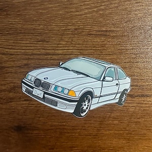 May include: A white sticker of a white BMW 3 series car with a blue and white BMW logo and the word "Drift" on the license plate.