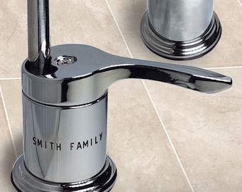 May include: Chrome bathroom faucet handle with a lever and a base that says "SMITH FAMILY".