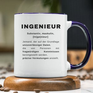 Könnte beinhalten: Weiße Keramiktasse mit blauem Rand und Henkel. Die Tasse hat eine Definition des Wortes "Ingenieur" in schwarzer Schrift darauf gedruckt. Die Tasse steht auf einem Untersetzer aus Holz.
