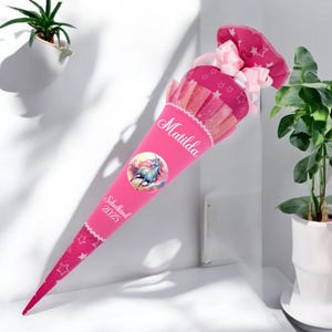 Könnte beinhalten: Rosa-weißer Schultüte mit Einhorn-Motiv und dem Text "Schulkind 2023" und "Matilda".