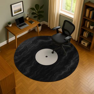 Puede incluir: Una alfombra redonda diseñada para parecerse a un disco de vinilo. La alfombra es principalmente negra con un centro blanco y un patrón texturizado. Una silla de oficina negra está sobre la alfombra, con un escritorio y una estantería de madera en el fondo.