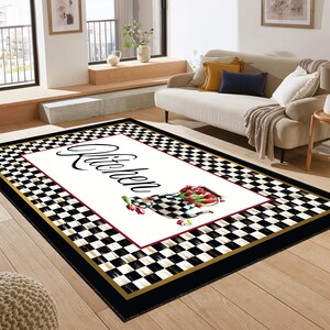 Black and white checkered kitchen rug with a gold border and a white rectangle in the center. The rectangle has the word "Kitchen" written in black cursive script and a red and white floral design.