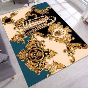 May include: A decorative rug with a gold and black design featuring intricate floral patterns and a pearl necklace. The rug has a teal border.