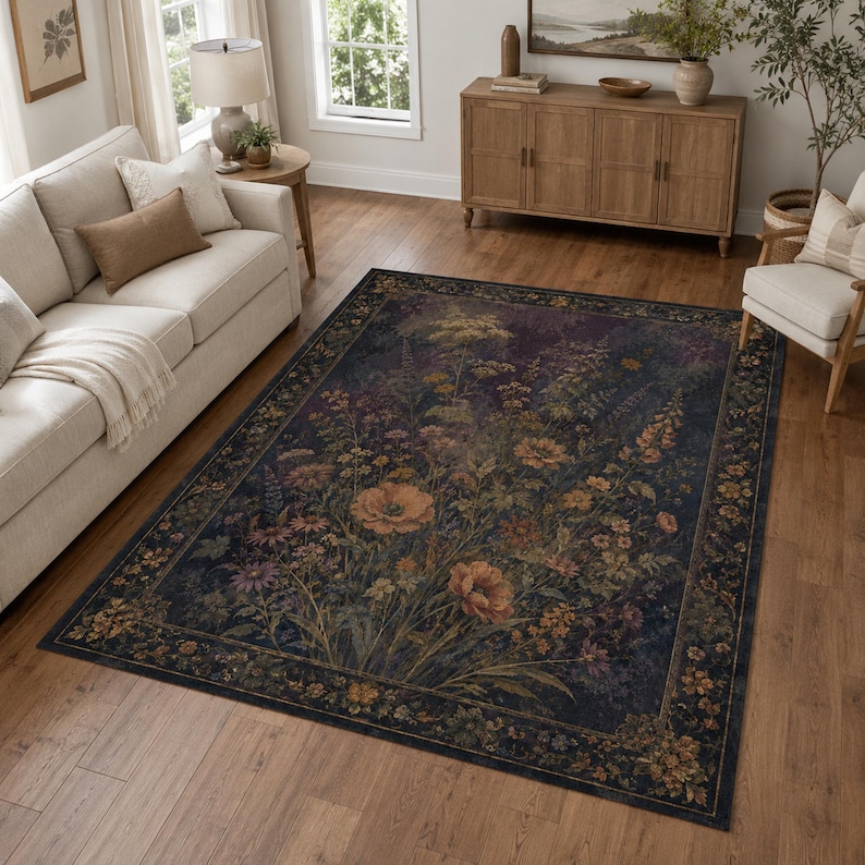 A rectangular area rug featuring a dark navy blue background with a central botanical print of wildflowers in shades of orange, yellow, and muted green. The rug has a wide decorative border with a repeating floral pattern throughout.