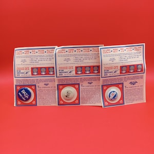 Puede incluir: Tres exhibidores de botones de campaña vintage sobre un fondo rojo. Cada exhibidor presenta una serie de pequeños botones plateados y un botón más grande con texto e imagen. El texto dice "HATS OFF TO THE PAST" y "CHOOSE ONE".