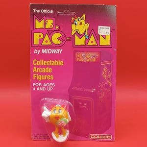May include: A Ms. Pac-Man collectible arcade figure by Midway, packaged on a pink and yellow card. The figure is in a clear plastic bubble. The card features the Ms. Pac-Man logo and arcade cabinet illustration. The text reads "Collectable Arcade Figures FOR AGES 4 AND UP."