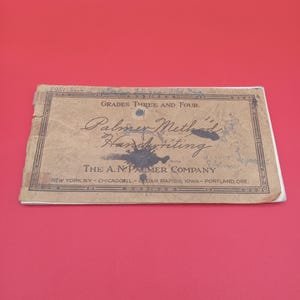May include: A vintage handwriting instruction book titled "Palmer Method Handwriting" for grades three and four. The cover is tan with black text and decorative elements. The book is from The A. N. Palmer Company, with locations listed.