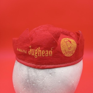 Puede incluir: Sombrero de fieltro rojo con un logotipo de Jughead bordado en oro y las palabras "Archie's Pal" en la parte delantera.