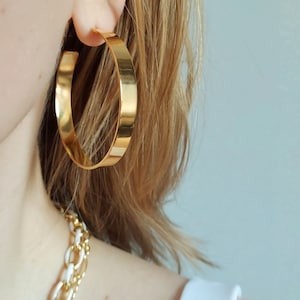 Op de afbeelding: Gouden creolen met een dikke, platte band. De oorbellen zijn groot en rond.