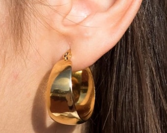 May include: Gold hoop earrings with a thick, rounded design. The earrings are worn in a person's ear.