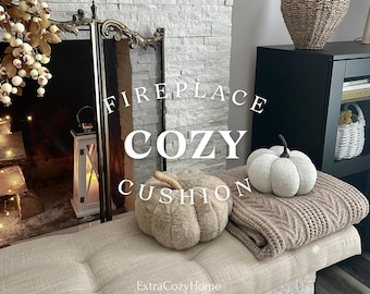 Könnte beinhalten: Ein Kamin mit einem gemütlichen Kissen in Form eines Kürbisses. Das Kissen ist braun und flauschig. Rechts neben dem Kissen liegt ein weißer Kürbis. Der Text "Fireplace Cozy Cushion" ist auf dem Bild zu sehen. Der Text "ExtraCozyHome" ist unten auf dem Bild zu sehen.