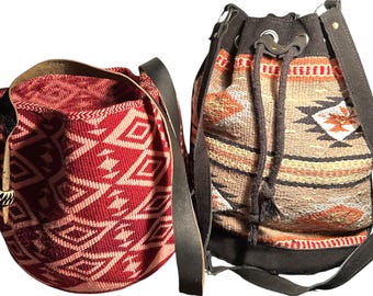 May include: Two bucket-style bags with shoulder straps. One is red with a geometric pattern, the other is tan with a Southwestern design. Both bags have drawstring closures and leather straps.