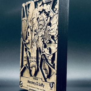 Op de afbeelding: Houten lasergesneden kaart met een gedetailleerde illustratie van een personage uit de anime-serie One Piece. De kaart heeft een zwarte rand en bevat de tekst "5000" en "Menkey.D.Luffy". De kaart wordt op een transparante standaard gepresenteerd.