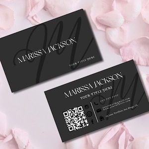 May include: Two black business cards with white text and a large stylized letter "M". The cards display the name "Marissa Jackson" and contact information, including a QR code and social media icons. The cards are on a pink petal background.