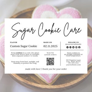 Könnte beinhalten: Herzförmige Zuckerkekse mit rosa und weißer Glasur auf einem Holztablett. Eine weiße Karte mit schwarzem Text liest sich "Sugar Cookie Care" und enthält Aufbewahrungshinweise. Der Geschmack ist "Custom Sugar Cookie".