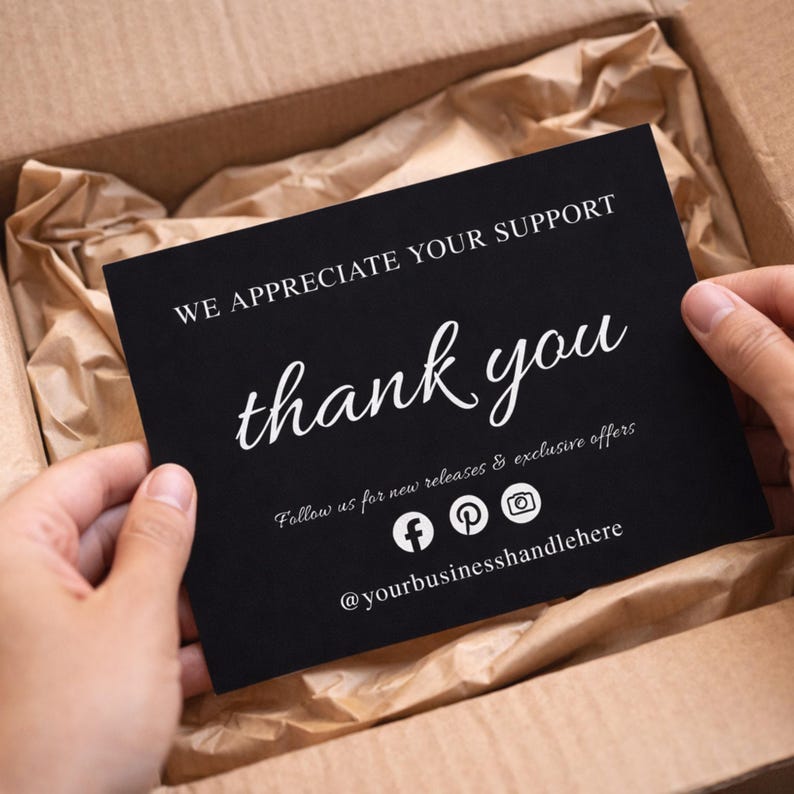Puede incluir: Una tarjeta negra con texto blanco que dice "WE APPRECIATE YOUR SUPPORT" y "thank you" en cursiva. La tarjeta tambi&eacute;n incluye iconos de redes sociales y el identificador @yourbusinesshandlehere. La tarjeta se sostiene en una caja de cart&oacute;n.