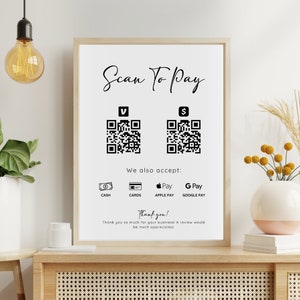 May include: A white sign with black text that reads "Scan To Pay".  Two black and white QR codes are displayed, one labeled "V" and the other labeled "$".  Below the QR codes, the sign reads "We also accept:" and lists the following payment methods: "Cash", "Cards", "Apple Pay", and "Google Pay".  The sign concludes with "Thank you! Thank you so much for your business! A review would be much appreciated."