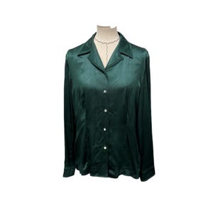 May include: A long-sleeved button-down shirt in a deep forest green color with a smooth, satin-like finish. The shirt features a classic pointed collar, a front button placket with four visible buttons, and cuffed sleeves, presented on a mannequin.