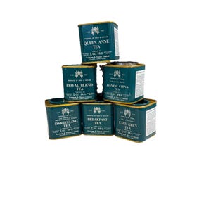 May include: A collection of six teal-colored tea tins stacked on top of each other. Each tin is labeled with a different tea type, including "Queen Anne Tea," "Royal Blend Tea," and "Jasmine China Tea." The tins are labeled with the text "Produce of India & Ceylon."