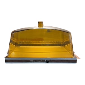 May include: A rectangular food warmer with a transparent amber-colored plastic dome lid. The base features a dark wood-grain finish with the brand name Cornwall printed in white, along with a black control knob for low, medium, and high settings.