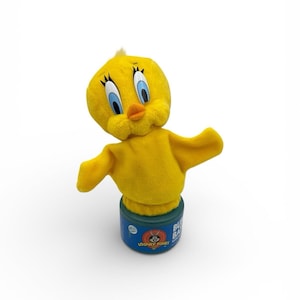 May include: A yellow Tweety Bird plush toy with blue eyes, an orange beak, and outstretched arms. The plush is attached to a blue and green base with Looney Tunes branding.