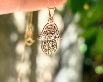 May include: Gold hamsa hand pendant necklace with intricate details. The pendant is a popular symbol of protection and good luck.