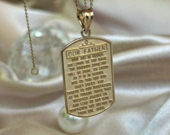 May include: A gold chain necklace with a gold pendant featuring the Lord's Prayer, "Our Father", engraved on a rectangular tag.