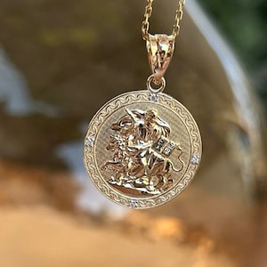May include: A gold pendant necklace with a round charm featuring a detailed image of a knight riding a horse. The charm is surrounded by a decorative border with small diamonds.