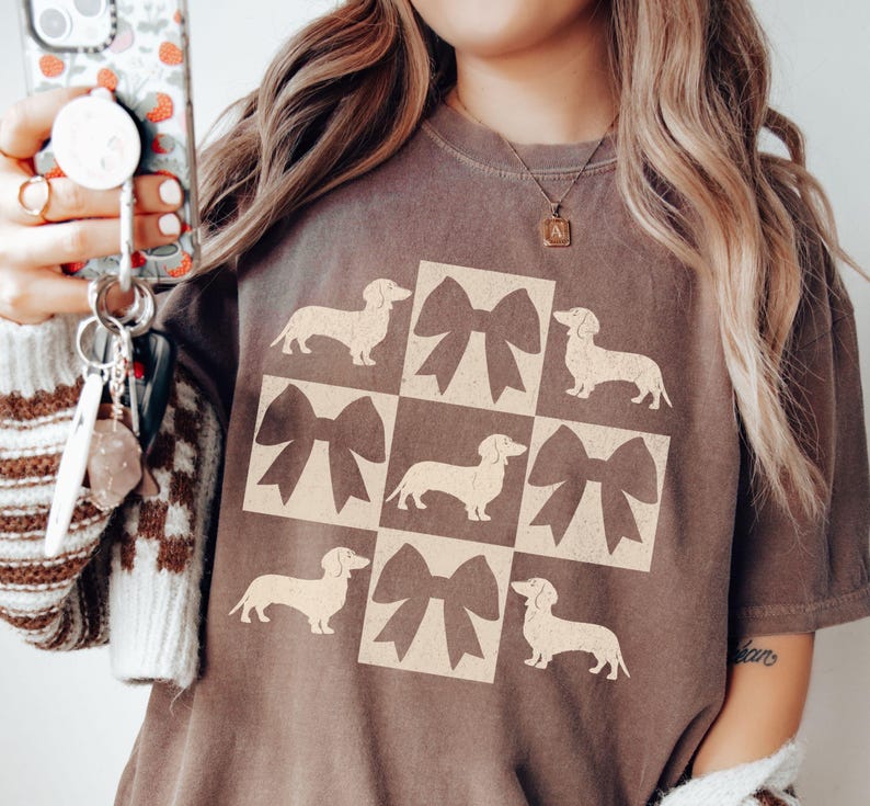 May include: A brown t-shirt with a graphic of a repeated pattern of dachshunds and bows. The graphic is in a cream color.