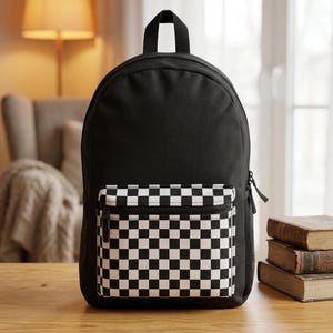 May include: A black backpack featuring a large main compartment and a smaller front pocket with a black and white checkered pattern. The bag includes a top handle, side mesh pockets, and black zipper pulls, providing a functional design.