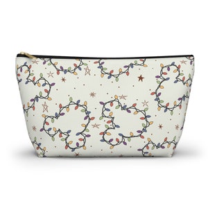 May include: Cream-colored zippered pouch with a repeating pattern of colorful string lights and star shapes. The lights are arranged in a Mickey Mouse head shape. The zipper is gold-colored.