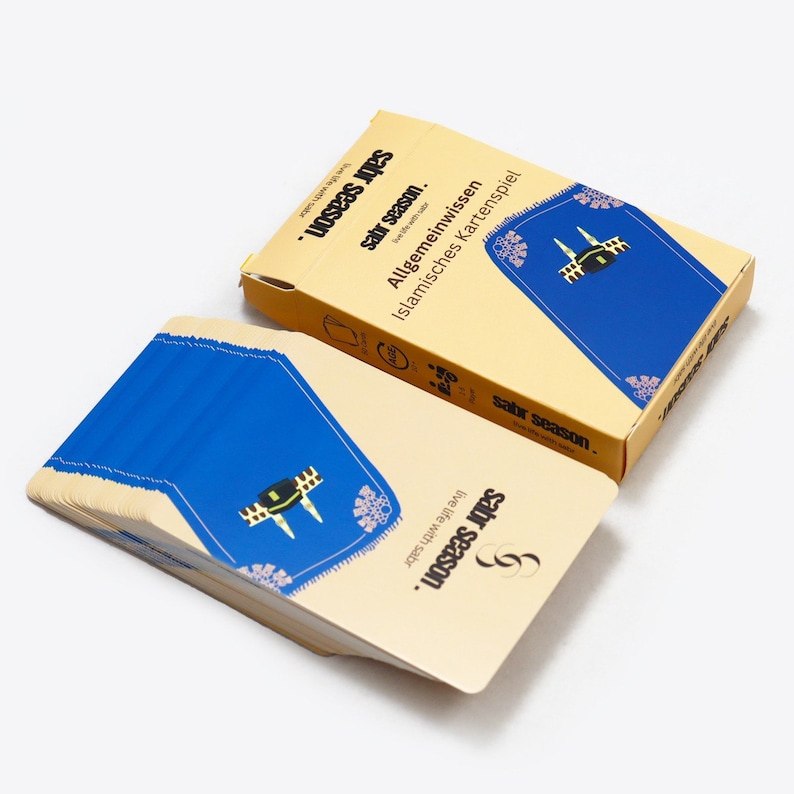 May include: A deck of cards with a blue and gold design. The box features the text "sabr season. live life with sabr" and "Allgemeinwissen Islamisches Kartenspiel".