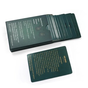 May include: A green box with a gold inscription that reads "Spielerisch dein Wissen testen" and a stack of green cards with gold lettering. The cards have instructions for a game about the life of the Prophet Muhammad.