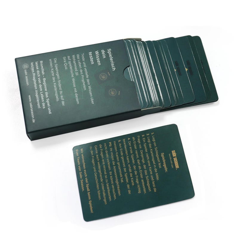 May include: A green box with a gold inscription that reads "Spielerisch dein Wissen testen" and a stack of green cards with gold lettering. The cards have instructions for a game about the life of the Prophet Muhammad.