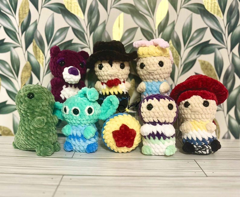 Puede incluir: Una colecci&oacute;n de juguetes de peluche tejidos a crochet, que incluye un dinosaurio verde, un extraterrestre azul, un oso rojo, un personaje morado y verde, un personaje rojo y amarillo, un vaquero, una princesa y un personaje rojo y amarillo con un sombrero rojo.
