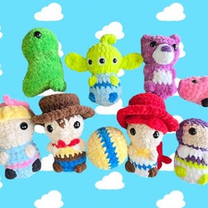 Puede incluir: Una colecci&oacute;n de juguetes de peluche tejidos a crochet inspirados en personajes populares. Los juguetes incluyen un dinosaurio verde, un extraterrestre de tres ojos, un oso morado, un cerdo rosa, una ni&ntilde;a rubia con un lazo rosa, un vaquero, una ni&ntilde;a con un sombrero rojo, una pelota amarilla y un extraterrestre morado.