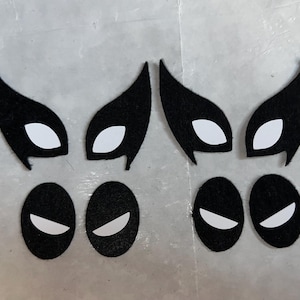 Könnte beinhalten: Sechs schwarze Filzmasken mit weißen Augenformen. Zwei der Masken haben eine spitze Form oben und zwei eine abgerundete Form. Die anderen beiden Masken sind oval.