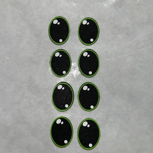 Pode incluir: Oito olhos saltitantes pretos e verdes com pupilas brancas. Os olhos estão dispostos em duas filas de quatro.