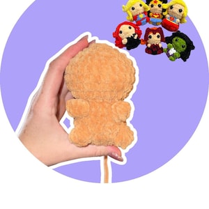 Peut inclure: Une figurine en crochet pelucheux beige avec une tête arrondie et de petits membres, accompagnée d'une collection de six petites poupées en crochet sur le thème des super-héros avec des tenues, des couleurs de cheveux et des designs variés.